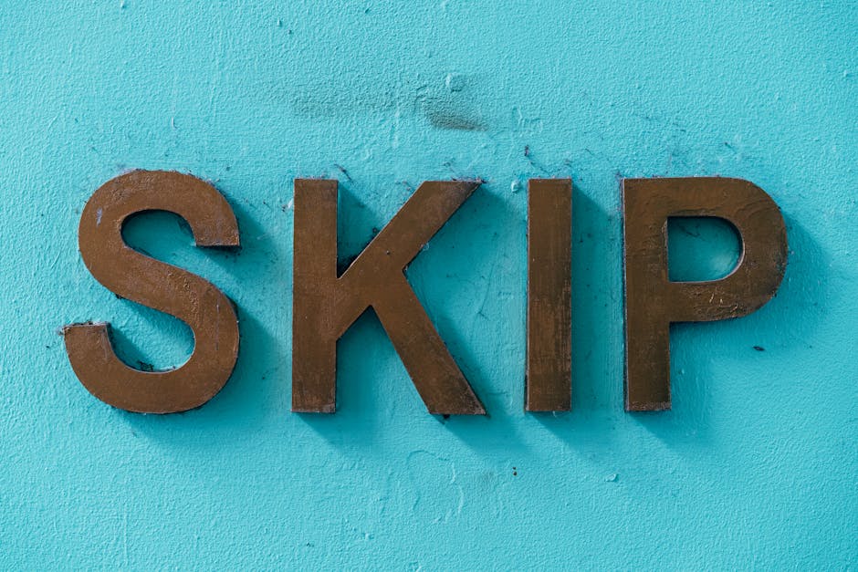The image features three large, metallic letters spelling 'SKIP' mounted on a textured, light blue wall. The letters have a matte, dark bronze finish with visible slight rust spots and a rough surface
